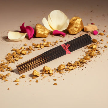 Amber White Incense Sticks with a pink ribbon on a beige background with gold pieces and flowers.