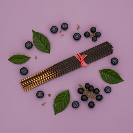 Imported Blueberry Grapes Incense Sticks with a pink ribbon surrounded by blueberries and leaves on a pink background