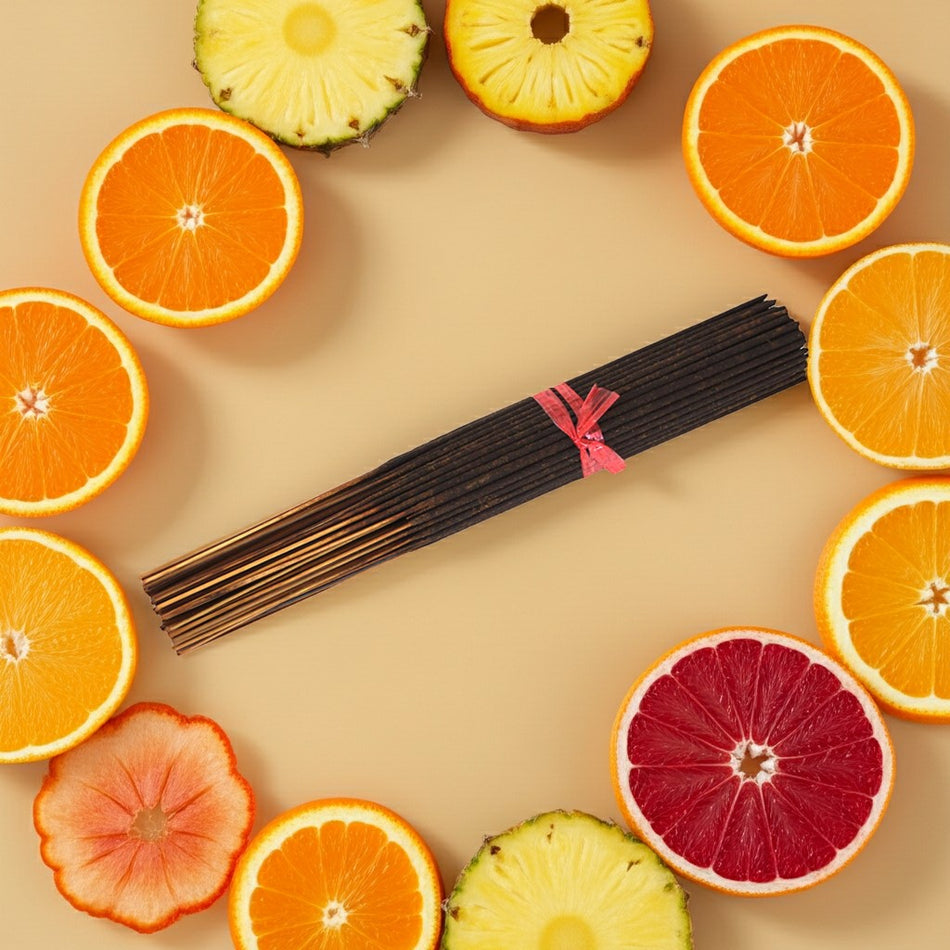 Jamaican Fruit Incense Sticks with a pink ribbon surrounded by sliced oranges, pineapples, and grapefruits on a beige background