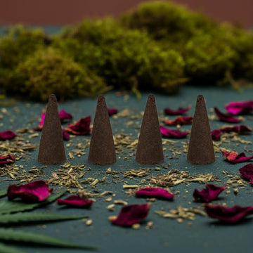 Kush Incense Cones on a dark surface with dried leaves and flowers, against a blurred natural background.