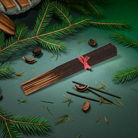 Pine Needles Incense Sticks with a pink ribbon on a green surface with pine branches