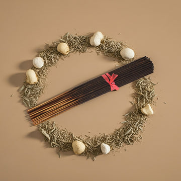 Desert Sage Incense Sticks with a red ribbon on a wreath of dried herbs and stones against a beige background