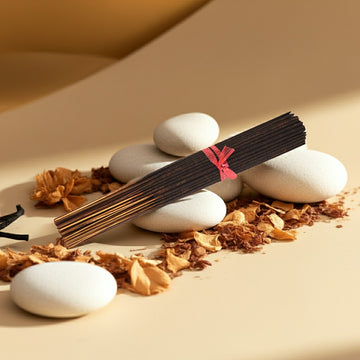 French Vanilla Incense Sticks with a pink ribbon on white stones surrounded by dried leaves on a beige background