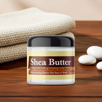 Jar of Amber White Scented Shea Butter on wooden surface with towels and stones in the background.