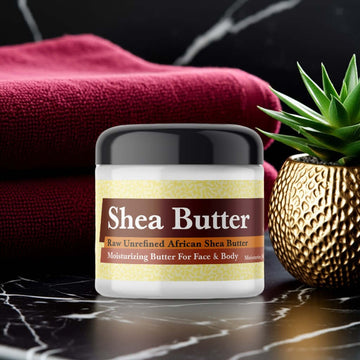 Jar of Bath & Body Into the Night Inspired Scented Shea Butter on a marble countertop with a red towel and potted plant.